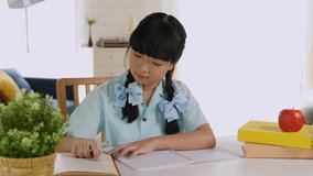 Happy homeschool Asian little young girl student learning and homework sitting on table at home.