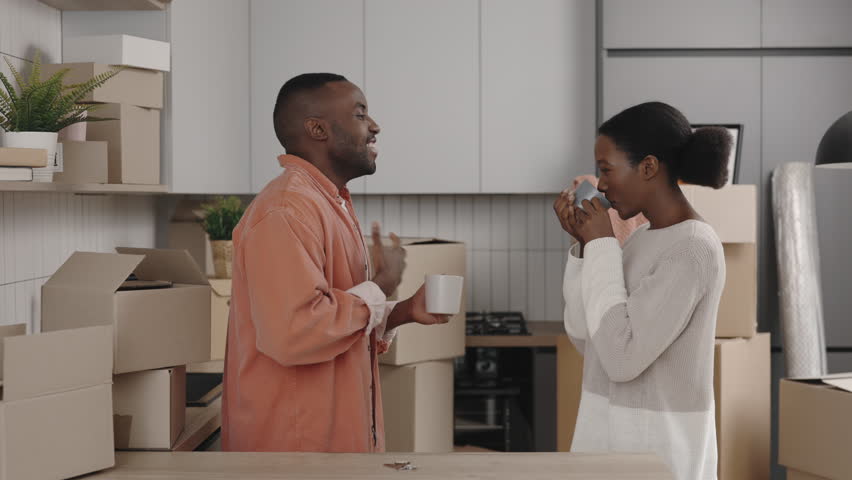 African american couple is happy to move into new flat drinking tea or coffee. Couple is talking about their new home and drinking tea. Family lifestyle and housing concept | Shutterstock HD Video #1098733805