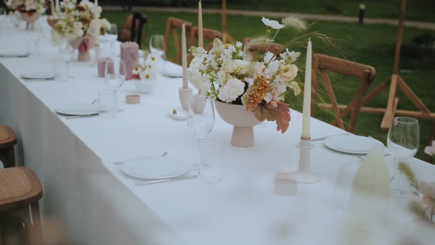 Close-up wedding table setting with pastel wild flowers, candles, old fashioned chairs and retro lamps on the background at small wedding party, slow motion. | Shutterstock HD Video #1098733847