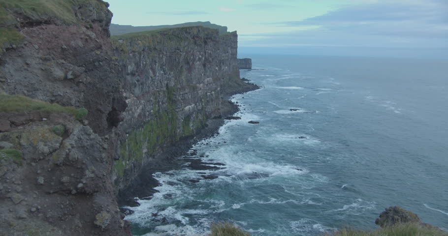 Icelandic cliffs at the westernmost point of europe.  Powerfull waves crashing against the steep rocky cliffs. Hiking at the boarder of europe. Green moss dn grass on rocks. Slow motion 60fps 4K DCI 