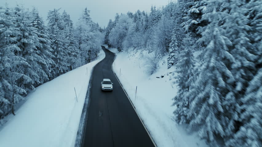 Cinematic and epic shot of beautiful winding mountain road in winter snow covered landscape. Winter season scenery on cloudy cold day. Car drive on small empty road in snowy forest wonderland | Shutterstock HD Video #1098739141