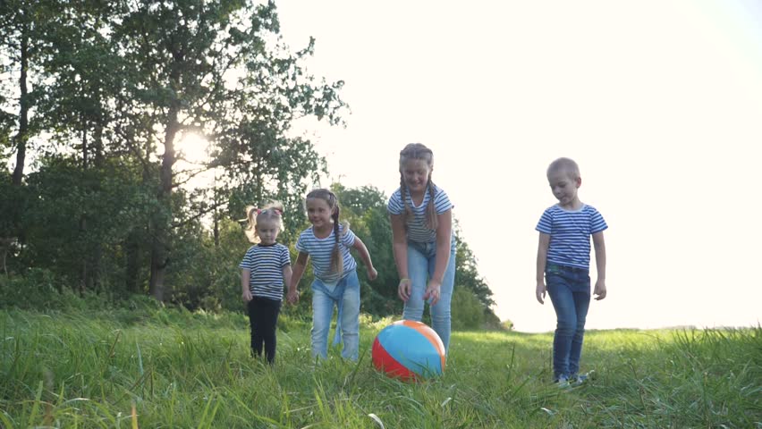 Happy family of children has fun in the park. Children with a crowd run for a colorful ball, catching up. Kids at sunset in the park have fun playing. Team game girls and boy. Royalty-Free Stock Footage #1098740631
