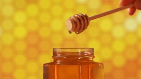 Woman hand getting honey from a jar with a wood dipper. Close up view of this healthy food made by bees in nature, acacia tree honey filmed in 4k video slow motion against honeycomb yellow background.
