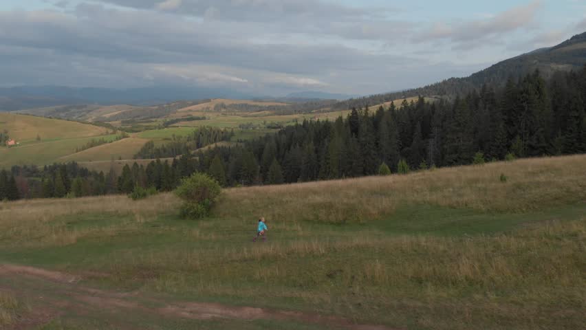Blond child walk with teddy bear in her hand climbing Carpathian mountains in western Ukraine. Drone follow