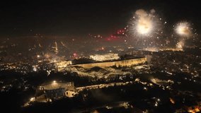 Aerial drone night rotational video of illuminated Acropolis hill and the Parthenon during New Year's eve 2022 with beautiful fireworks exploding, Athens historic centre, Attica, Greece