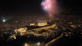 Aerial drone night rotational video of illuminated Acropolis hill and the Parthenon during New Year's eve 2022 with beautiful fireworks exploding, Athens historic centre, Attica, Greece