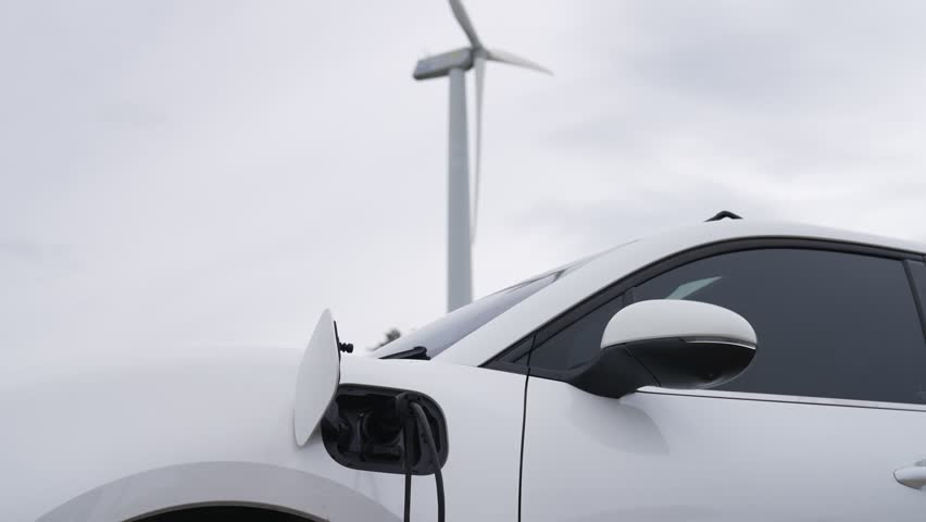Progressive future energy infrastructure concept of electric vehicle being charged at charging station powered by green and renewable energy from a wind turbine in order to preserve the environment. | Shutterstock HD Video #1098745207