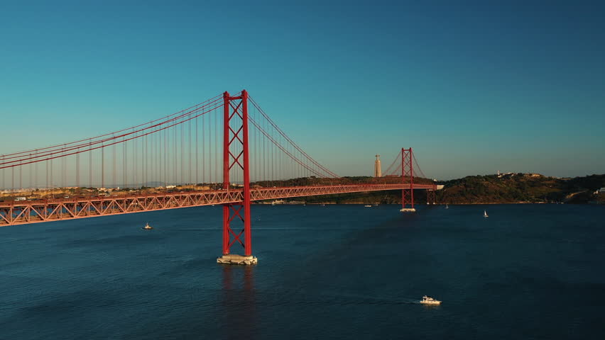 Golden hour views of the 25 de Abril Suspension Bridge over Tagus river in Lisbon, the capital of Portugal, with busy traffic on the bridge during sunset hours. Royalty-Free Stock Footage #1098746935