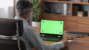Businessman has video call on laptop green screen with tracking markers. Male worker showing results of work on graphs and diagrams during video conference. Over shoulder laptop screen view.