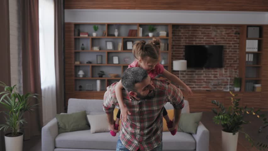 Happy family. Young father and cute daughter playing together fly as airplane. Dad and child having fun with piggyback ride at home. Enjoy spending time together, home leisure. Father's day. Royalty-Free Stock Footage #1098747831