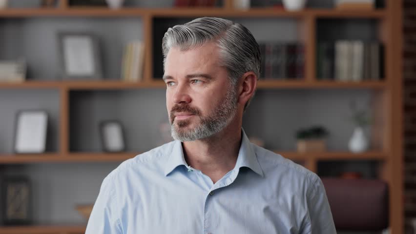 Business portrait of confident handsome bearded businessman looking at camera and smiling. Front close up portrait of Caucasian gray-haired man indoors at home office. Human face. Royalty-Free Stock Footage #1098747851
