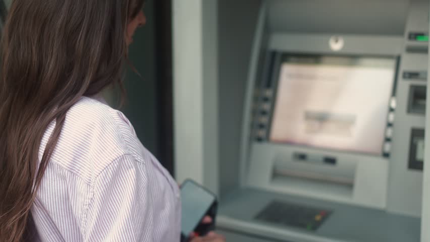 Back view of young caucasian female using ATM terminal withdrawing money on street. Adult woman making bank transactions cashing out holding receipt of bank operation. Finance concept. Royalty-Free Stock Footage #1098749077