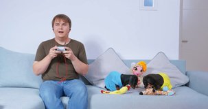 Family day off man enthusiastically plays video games in hands of joystick two dogs sit on sofa play with soft toys gnaw. Parenthood indifference lack of attention psychological trauma, game addiction