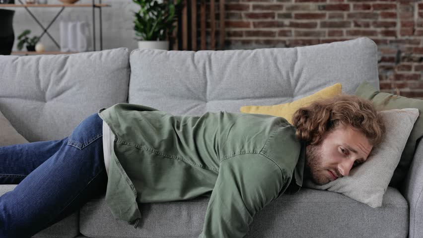 Exhausted overloaded man came home after work flopped down on couch feels like squeezed lemon. Concept of after party, tired overworked person hard day, lack of energy, breakdown. Tired lazy guy | Shutterstock HD Video #1098753799
