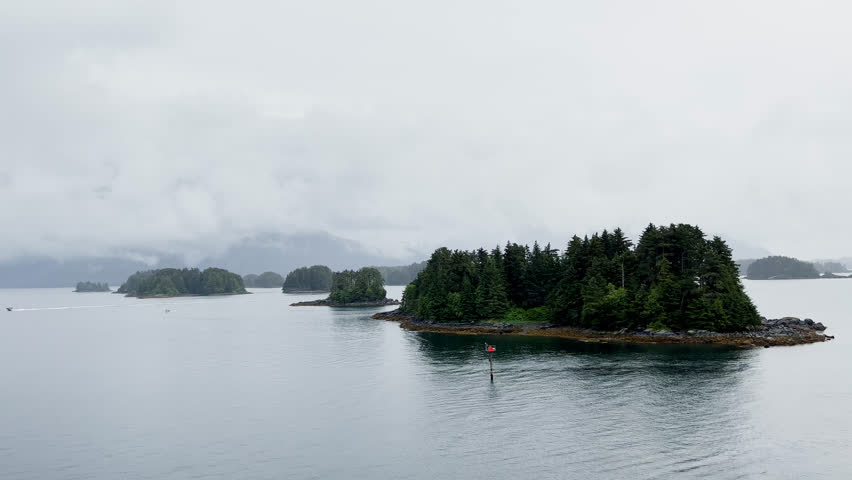 Tree covered islands in the Alaskan waters with fog covered mountains in the background on rainy and snowy day.