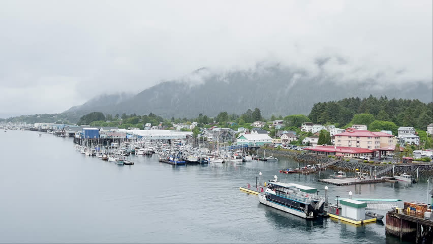 Boats docked in small town harbor in Alaska on cloudy day with fog covered mountains in the background