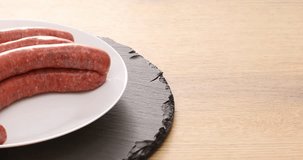  raw sausages on a white plate and stone tray. ready to fry. traditional cuisine. High quality 4k footage