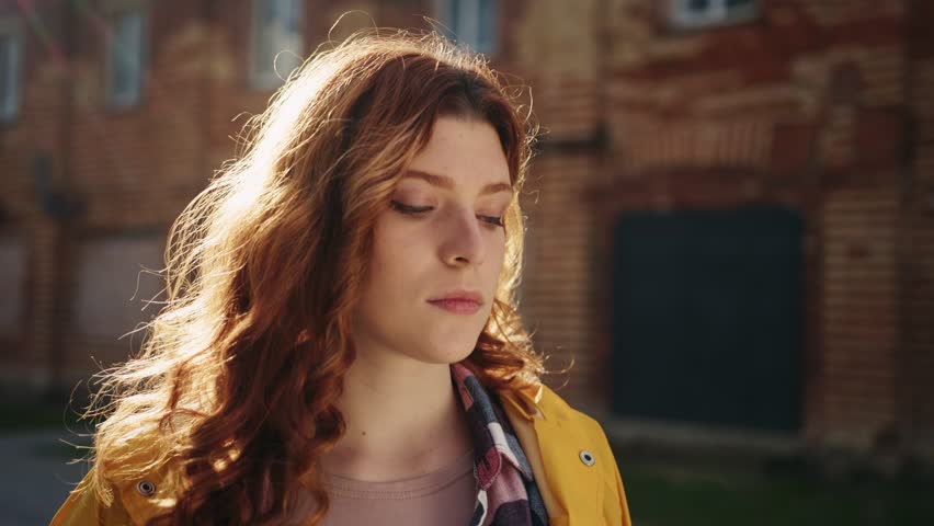 Footage of serious attractive redhead girl with long curly hair looking at camera. Young beautiful woman with green eyes. Blurred background of building. Sunlight. Daytime. Autumn colors. Outdoors Royalty-Free Stock Footage #1098760239