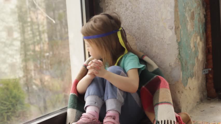 a little girl sits at the window and prays for peace in Ukraine.