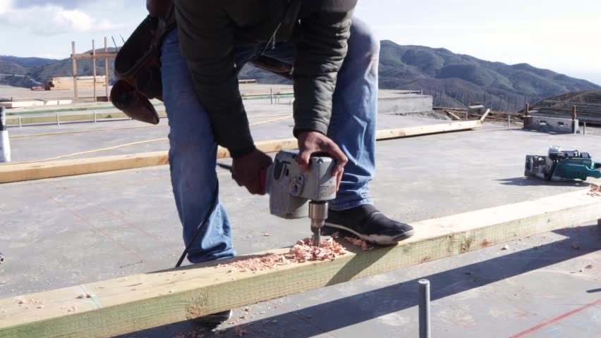 Worker uses a power tool to drill through a plank at construction yard., an Industrial Video by Redheart Entertainment