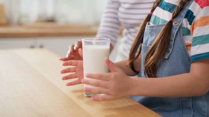 Caucasian little kid holding a cup of milk and drinking with mother. Attractive mom teach and support young girl daughter take care of her body, sipping a milk after wake up for health care in house. Royalty-Free Stock Footage #1098765673