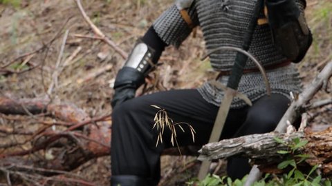 Smooth camera movement, selective focus, a man with gray hair and a scar on his face sits on a fallen tree with a two-handed sword in his hands. Medieval warrior, witcher in chainmail on a half. Arkivvideo