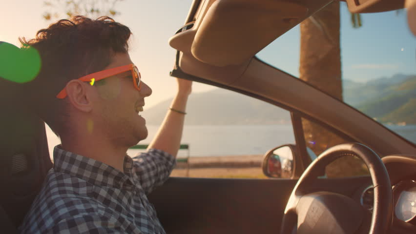 Careless relaxed man in sunglasses driving cabriolet car at fantastic golden sunset. Sun flare. Concept of success, tourism, rental cars. Happy smiling tourist travel in California. Summer vacation Royalty-Free Stock Footage #1098770423