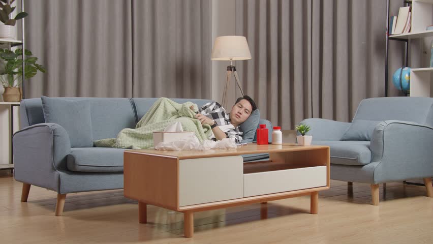 Asian Man With Blanket Suffering From Cough While Lying On Sofa In The Living Room At Home
