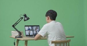Young Asian Male Waving Hand For Greeting And Speaking While Studying By A Laptop On Green Screen Background At Home
