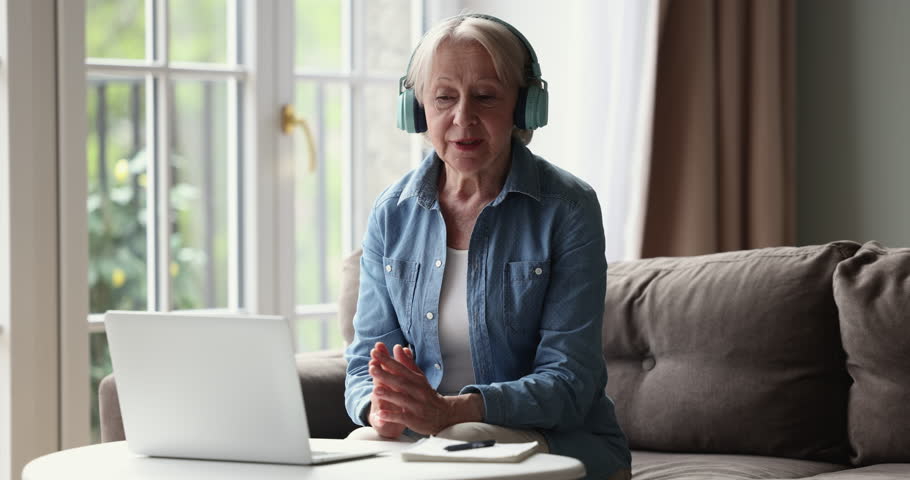 Senior female tutor wear headphones make video call communicates with learner use app, provided helpful information and knowledge, lead on-line class at home. Distancing conversation use wireless tech Royalty-Free Stock Footage #1098773639