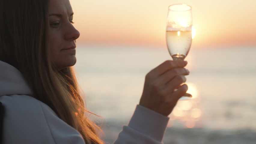 The girl turns a glass of Champagne in her hand, the sunrise on the sea, the reflection in the glass. Close-up. | Shutterstock HD Video #1098775107
