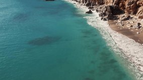 4K aerial drone footage of the turquoise waters of the ocean crashing against the rocky shore and foaming. Beautiful video of the sea surf in slow motion