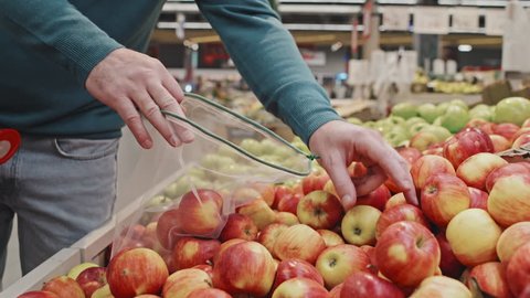 Unrecognizable couple of customers placing fresh apples in reusable produce bags while doing food shopping at supermarket Stock Video