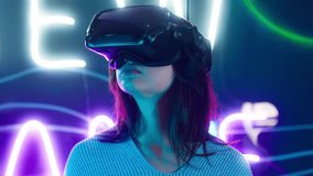 Cyber gamer in VR glasses plays virtual reality game in neon futuristic space. Cyberpunk fashion gaming concept. Man and woman play metaverse virtual digital technology game control with VR goggle.