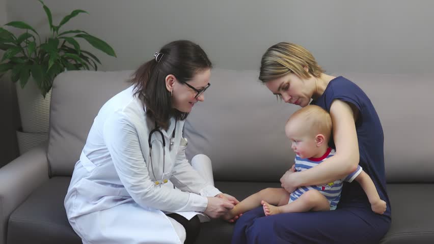 doctor woman visiting baby toddler at home, appointment mother and child home, doctor examines kids neck, ears, stomach, doing check-up stethoscope. mother holds son knees, sitting on sofa living room Royalty-Free Stock Footage #1098790581