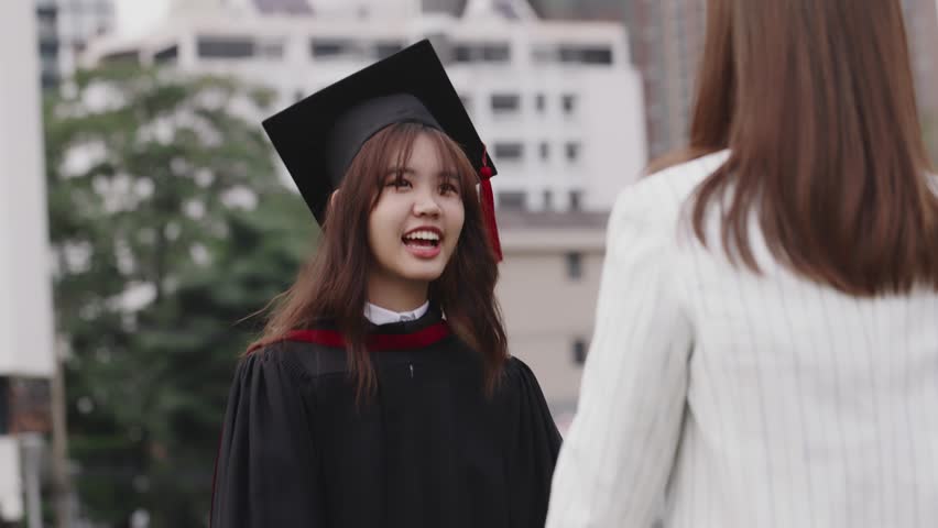 Happy Asian girl in graduation gowns with holding diploma are hugged mother by love and proud. Asian mom embraces daughter with joy on graduation day and successful. Royalty-Free Stock Footage #1098796433