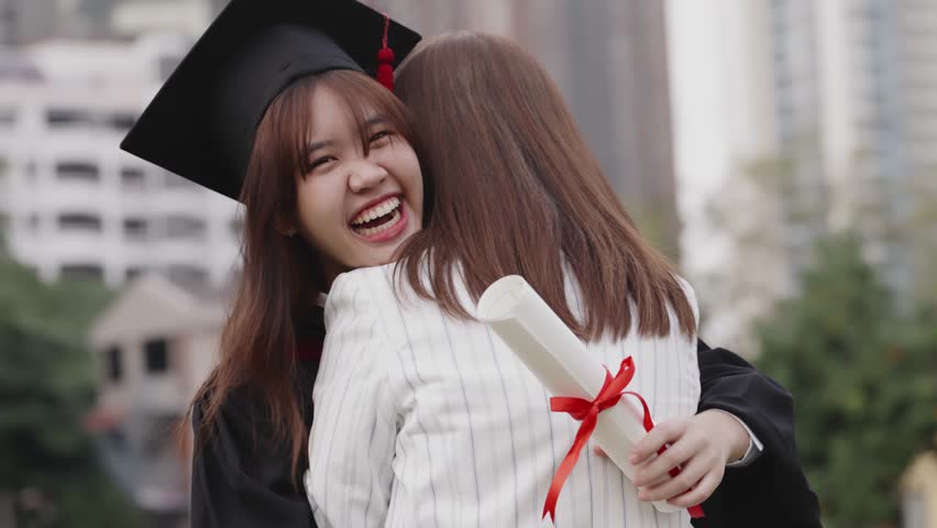 Happy Asian girl in graduation gowns with holding diploma are hugged mother by love and proud. Asian mom embraces daughter with joy on graduation day and successful. Royalty-Free Stock Footage #1098796433