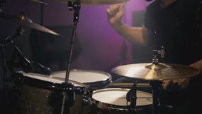A young Caucasian man drummer plays a drum kit in a music studio. Creates music and art. Drum set, drum kit in dark, drummer plays. The rock band is rehearsing, studying. The musician is playing
