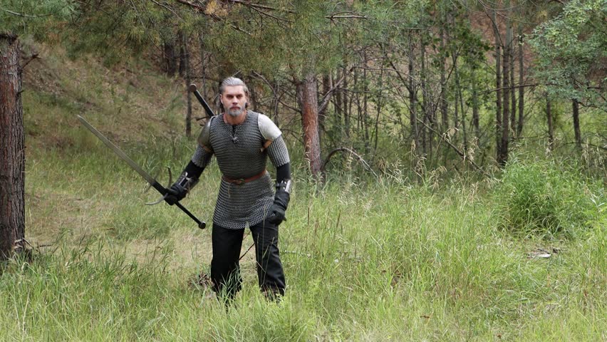 A medieval warrior with gray hair, dressed in chain mail with shoulder pads and a two-handed sword in his hands, carefully walks, crouching through the forest. Witcher, hunter of the Middle Ages