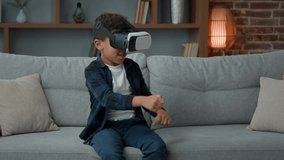 Funny little African American small ethnic boy kid child pupil schoolboy at home couch playing online video metaverse 3d game with VR glasses augmented virtual reality headset AR technology gaming 