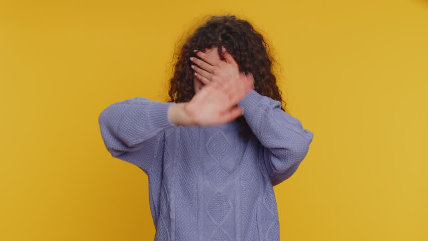 Dont want to look at ther, awful. Shocked millennial woman closing eyes with hand showing stop gesture, confused shy scared to watch. Young adult curly haired girl isolated on yellow studio background | Shutterstock HD Video #1098808607