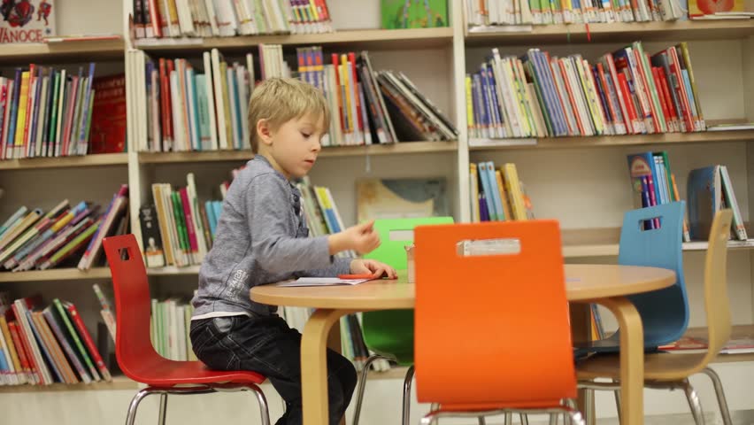 Adorable little child, boy, sitting in library, reading book and choosing what to lend, kid in book store