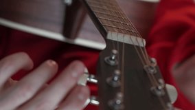 Vertical video. Guitar tuning. Male hobby. Instrumental skill. Closeup man adjusting pegs and gears on string with headstock light room interior blur.
