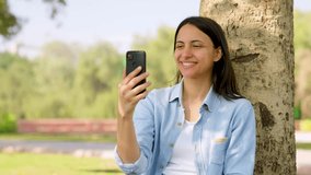 Happy Indian girl talking to someone on a video call in a park