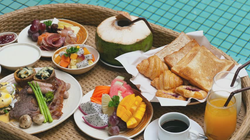 Delicious breakfast in straw tray on modern villa with swimming pool. Floating breakfast with fresh croissants, tropical fruits and juices. Luxurious travel, resort vacation, holidays in Thailand