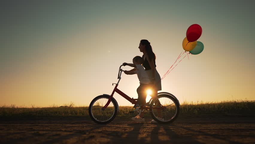 Happy family. Mom teaches son to ride bike. Concept of children holiday and dreams. Family playing in park at sunset. Silhouette of mom and son on a bike in the park. Green energy. Mom teaches son. Royalty-Free Stock Footage #1098814655