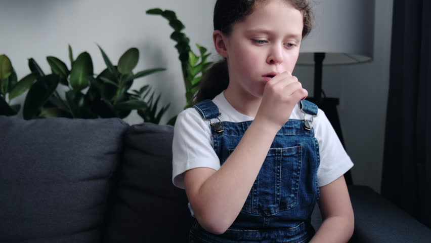 Close up portrait of unhealthy upset little girl kid sitting on grey sofa at home holding neck, suffering from painful feelings in throat, angina, hard to swallow, voice loss. Child immunity concept Royalty-Free Stock Footage #1098814807