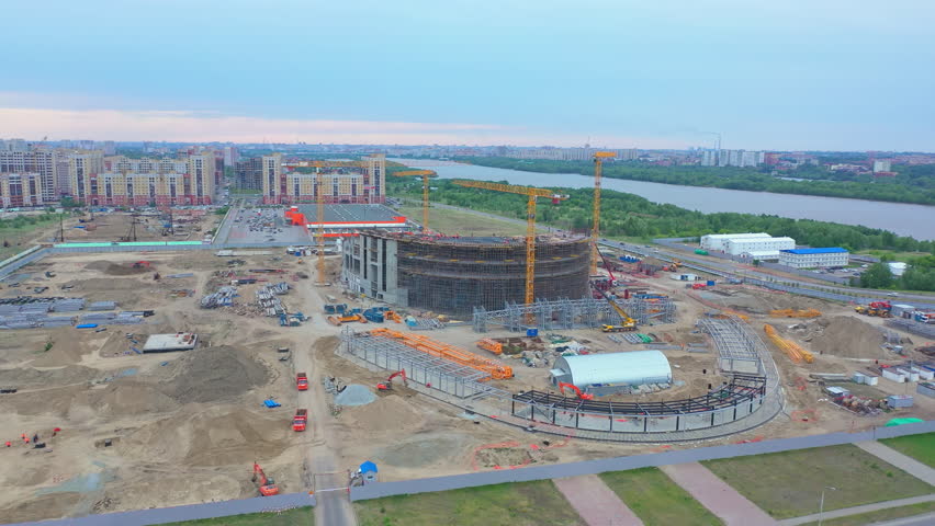 Future sports stadium and different machines with supplies at construction site on green riverbank by city bird eye view | Shutterstock HD Video #1098816139