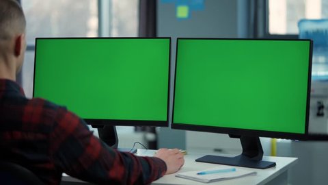 Young Man Working On Computer With Two Green Screen Mock Ups Sitting At Desk In Office วิดีโอสต็อก