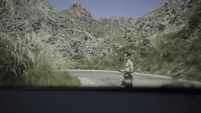 View of a shirtless athletic young man carrying a remote control in the middle of a mountain road.